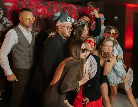 Goście weselni pozują z gadżetami na tle ścianki fotobudki